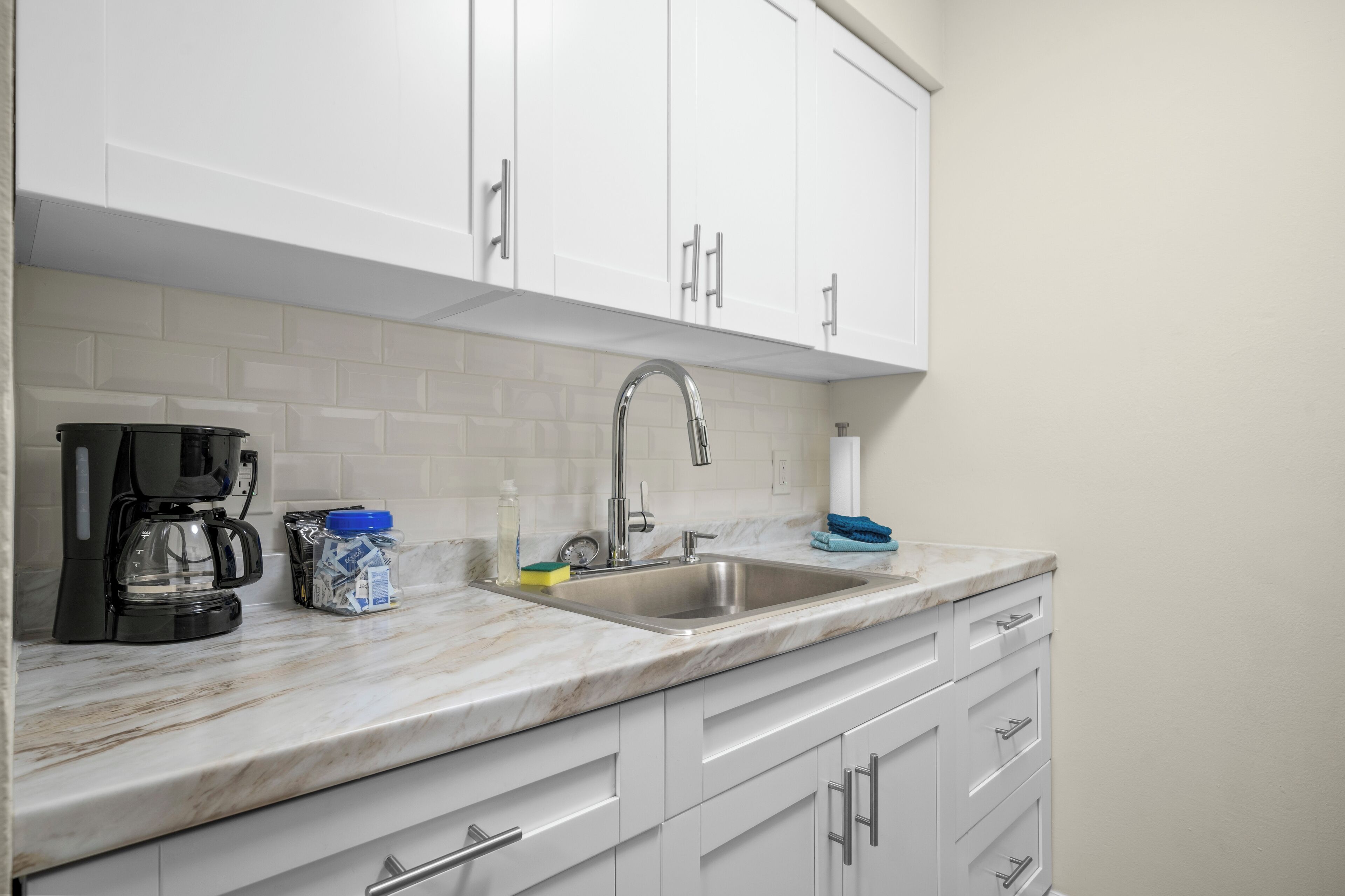 A modern kitchen with white cabinets, a stainless steel sink, and a marble countertop.