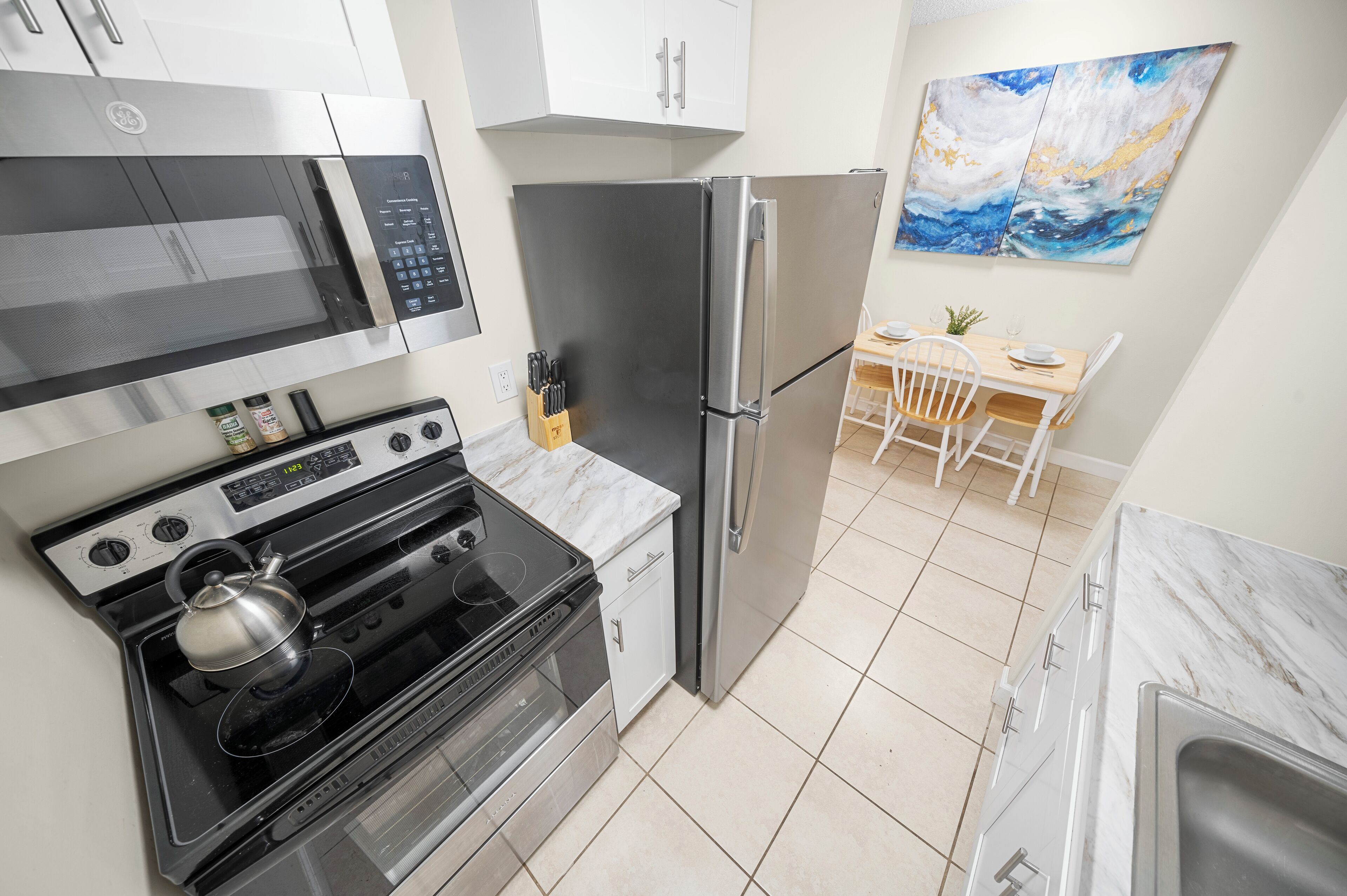 Una cocina moderna con un refrigerador de acero inoxidable, un microondas, un horno y un comedor con mesa y sillas de madera.