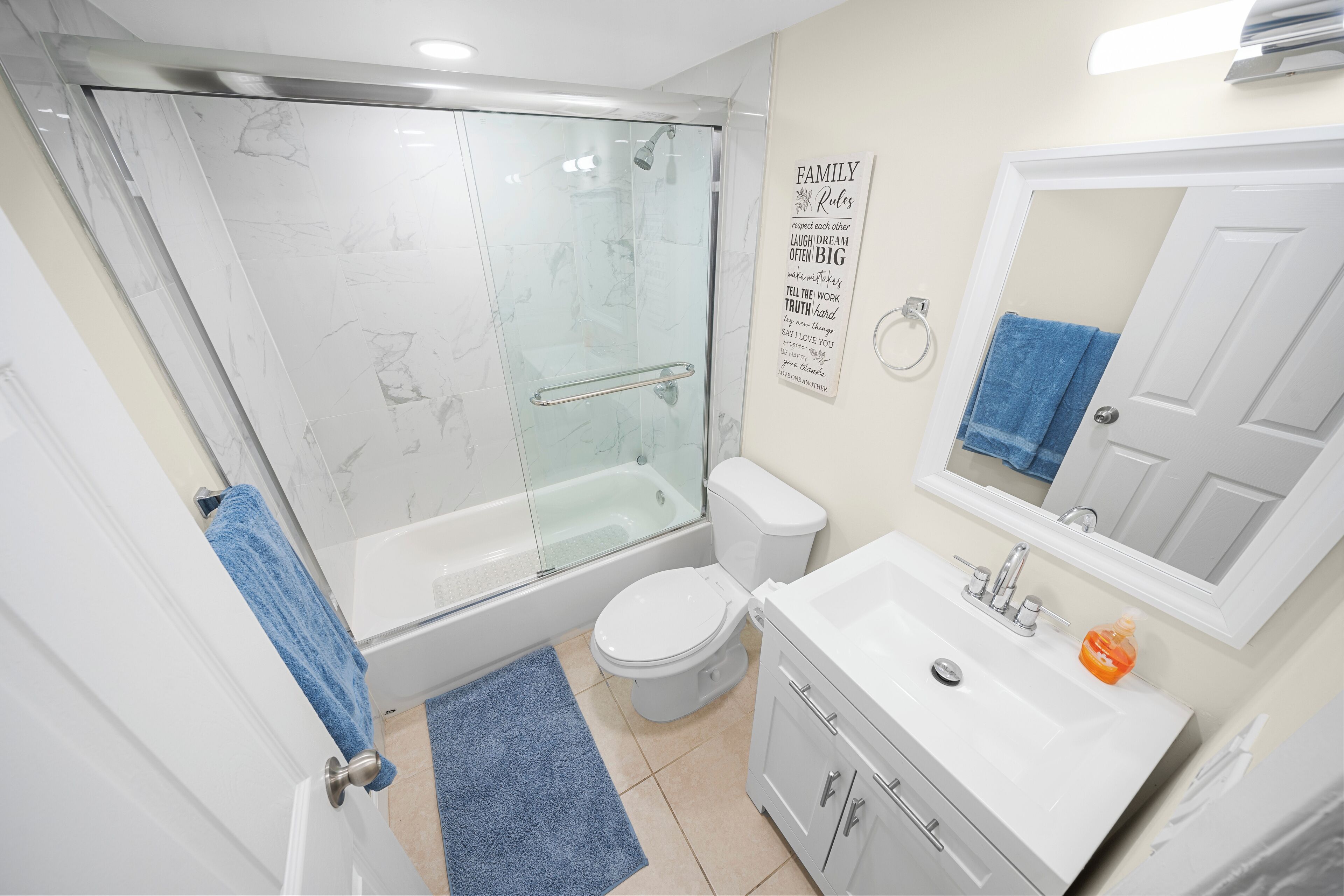 A modern bathroom with a glass-enclosed shower, a white toilet, a sink with a mirror, and a blue towel on the door.