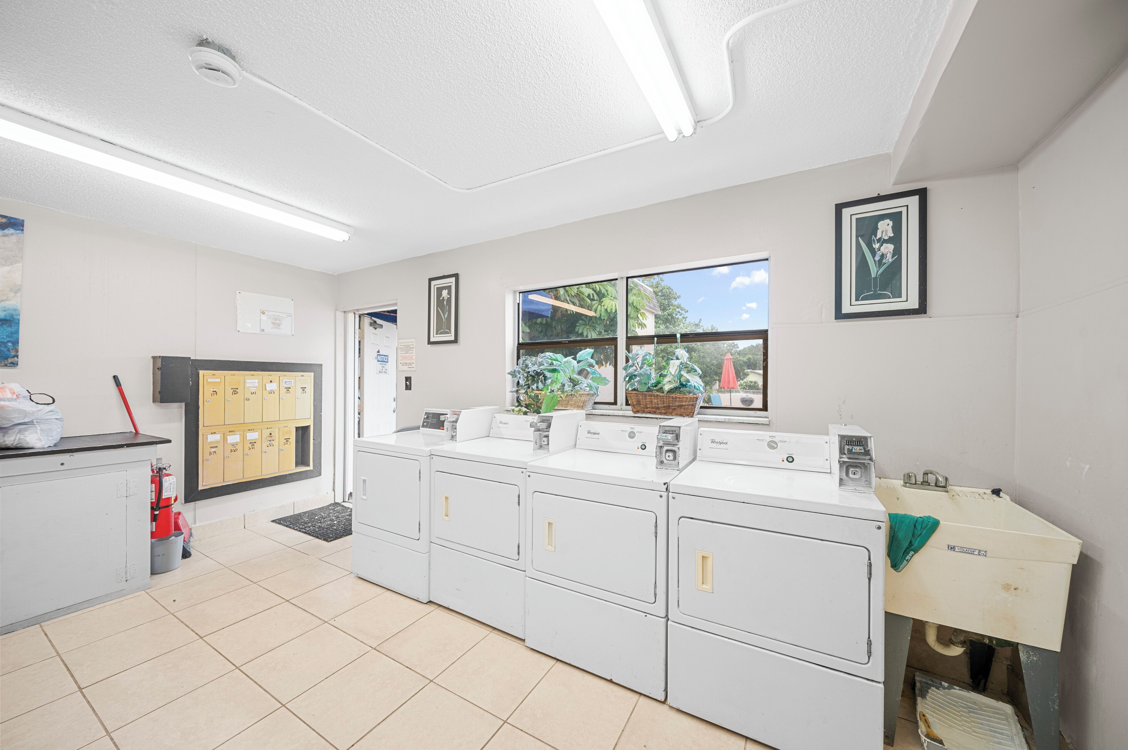 A laundry room with white cabinets, a washing machine, a dryer, a window with a view of greenery, and a fire extinguisher.