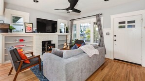 A living room with a grey sofa, a wooden chair, a fireplace, a TV, and a door with a window.