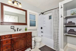 A bathroom with a wooden vanity, a large mirror, a bathtub, and a shower curtain. - Historic Craftsman Home in South Park near Zoo, Balboa Park, sleeps 8! (San Diego)