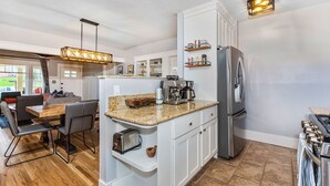 A modern kitchen with white cabinets, a granite countertop, a stainless steel refrigerator, and a coffee maker.