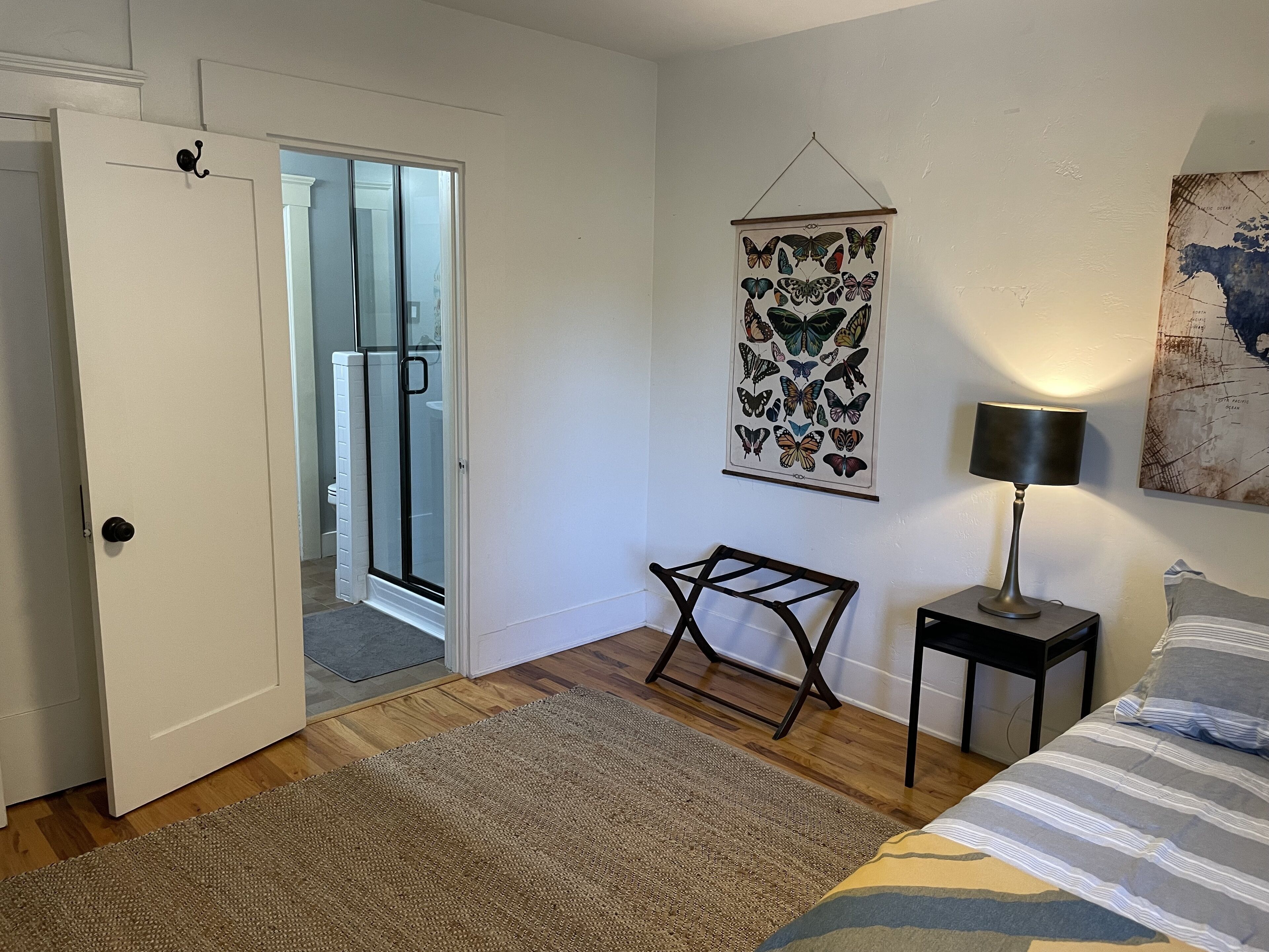 Un dormitorio con cama, mesita de noche, lámpara, un adorno de mariposas en la pared y una puerta que da a un balcón.