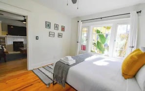 Ein Schlafzimmer mit Bett, einem Fenster mit Vorhängen, einem Kamin und einer Tür zu einem anderen Raum.