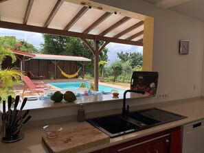A kitchen with a view of a swimming pool, outdoor seating, and a hammock.