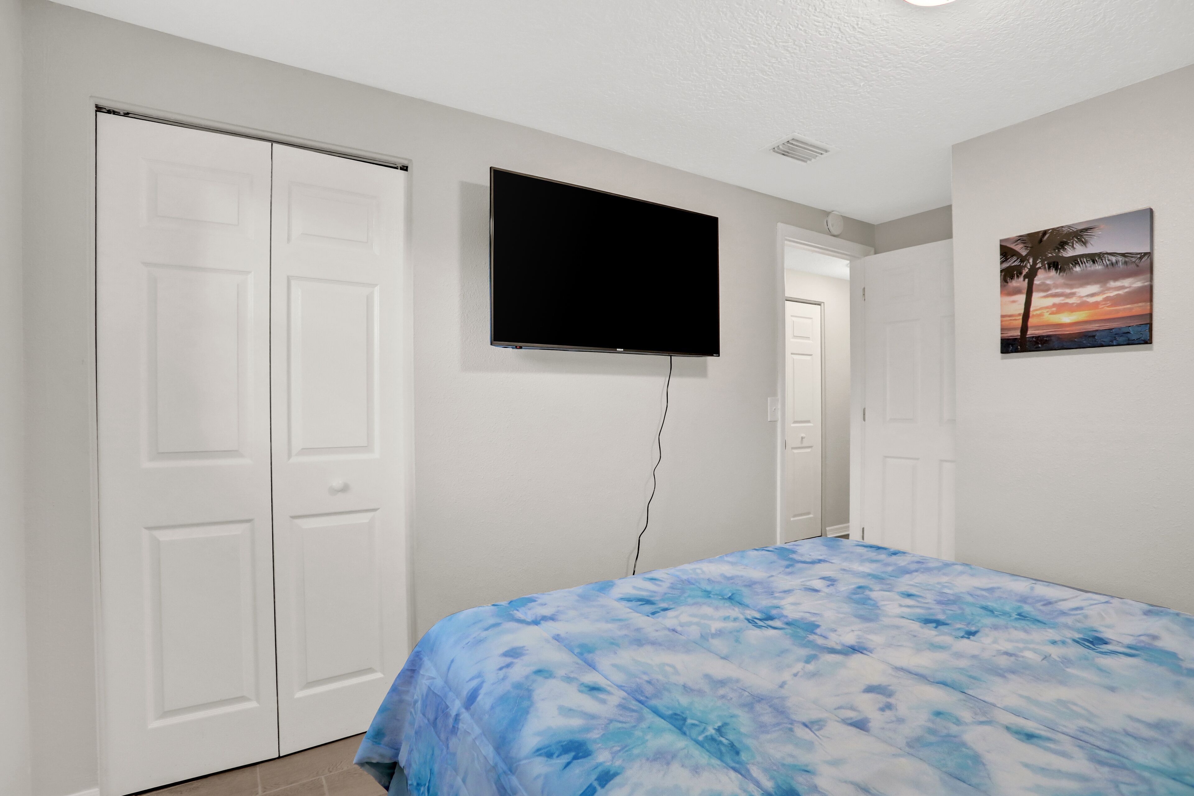 A bedroom with a bed, a TV mounted on the wall, and a door with a picture of a sunset.