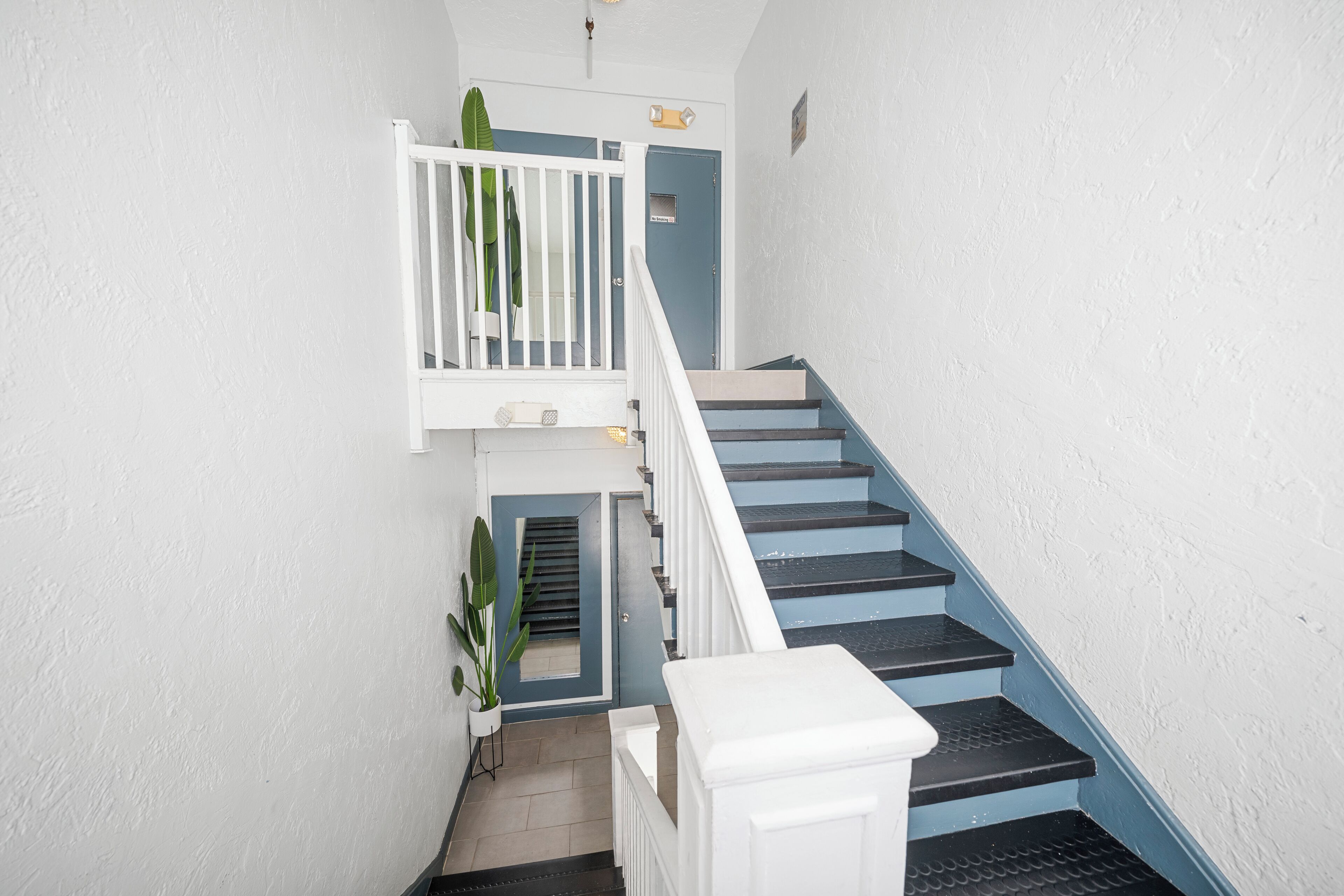 A staircase with white railings and blue steps, leading to a landing with a door and a small plant.