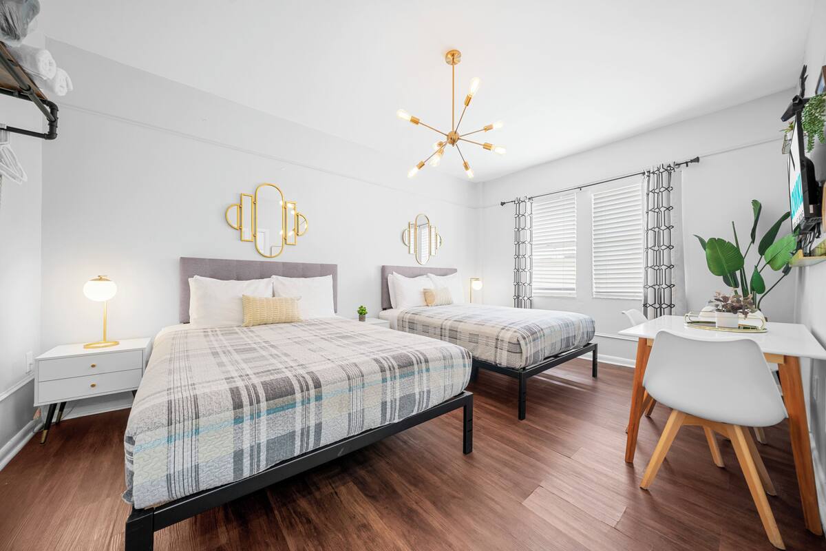 A modern bedroom with two beds, a desk, and a dining table.