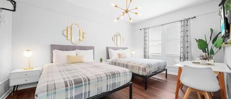 A modern bedroom with two beds, a desk, and a dining table.