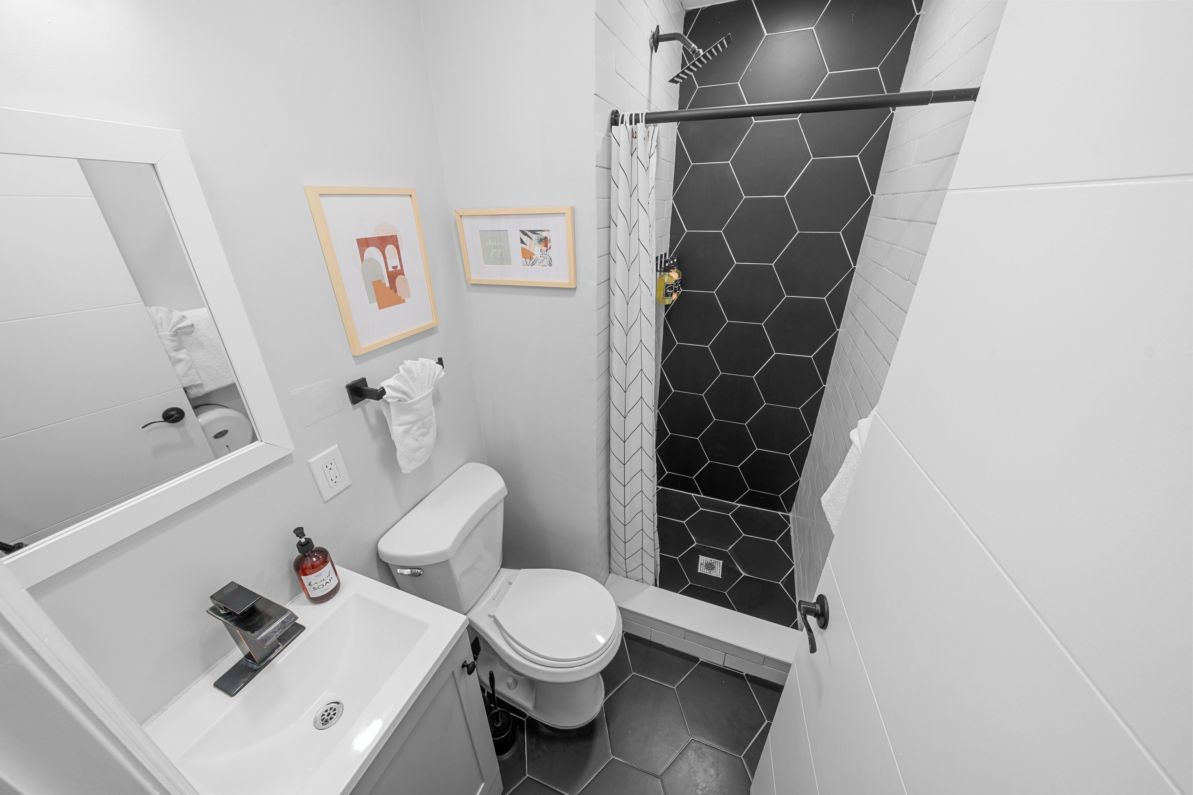 A modern bathroom with a white toilet, a sink, and a shower area with black hexagonal tiles.