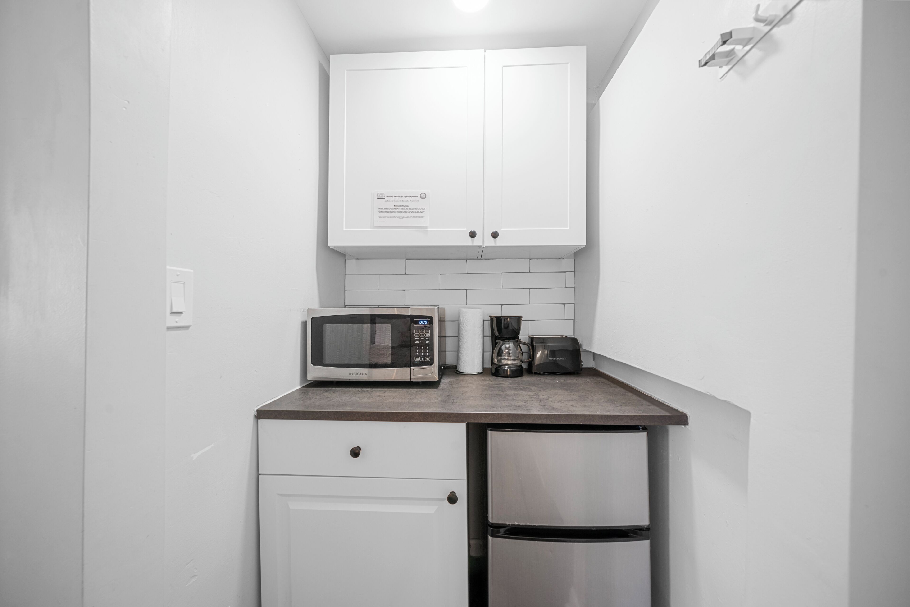 Una cocina compacta con armarios blancos, microondas, cafetera y refrigerador.