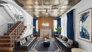 Un vaste espace de vie doté d’une cheminée, de canapés en cuir noir, d’un tapis à motifs et d’un escalier avec des rampes en métal.