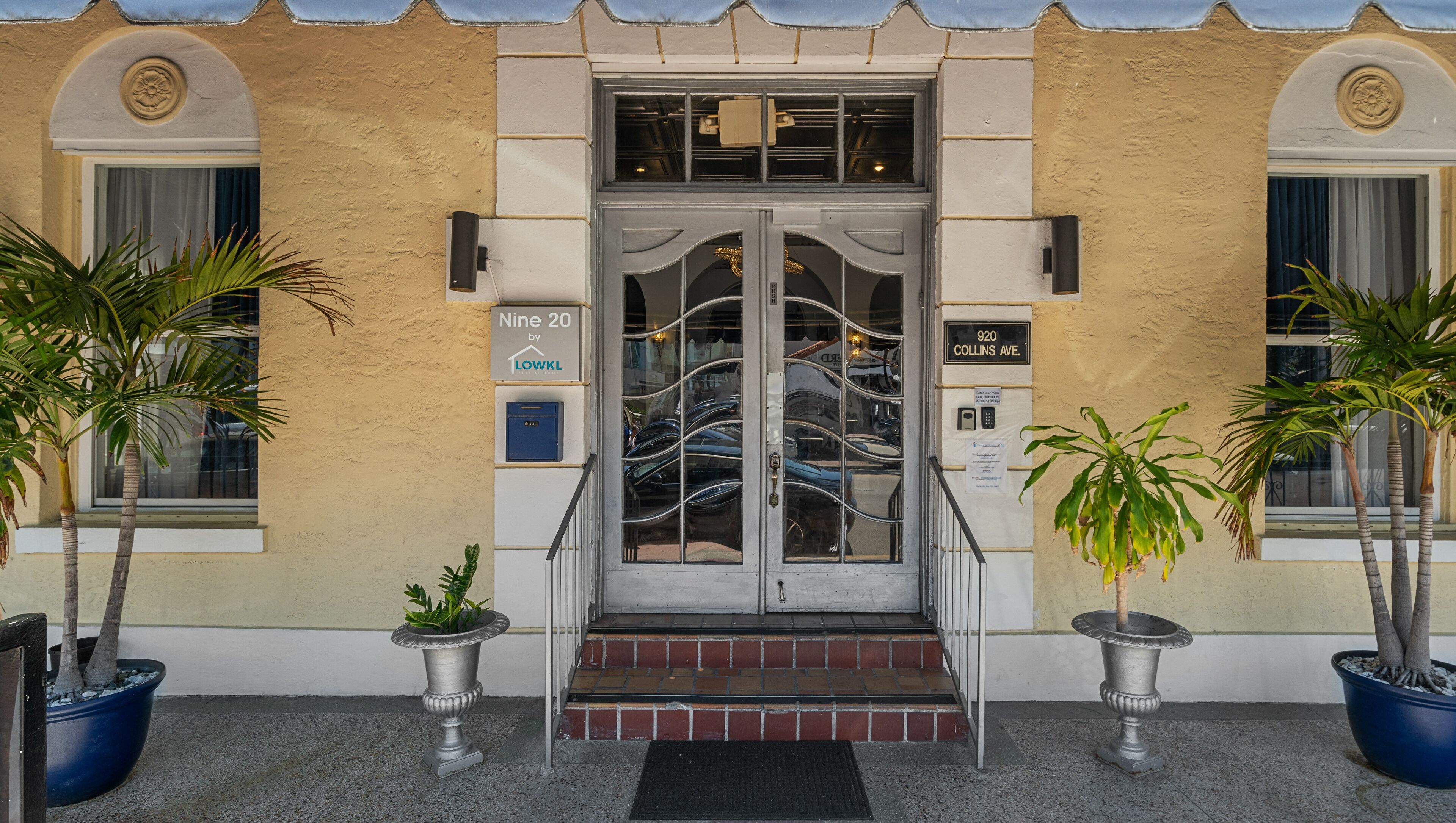 Entrada de um edifício com porta dupla, caixa de correio e placa com a inscrição 