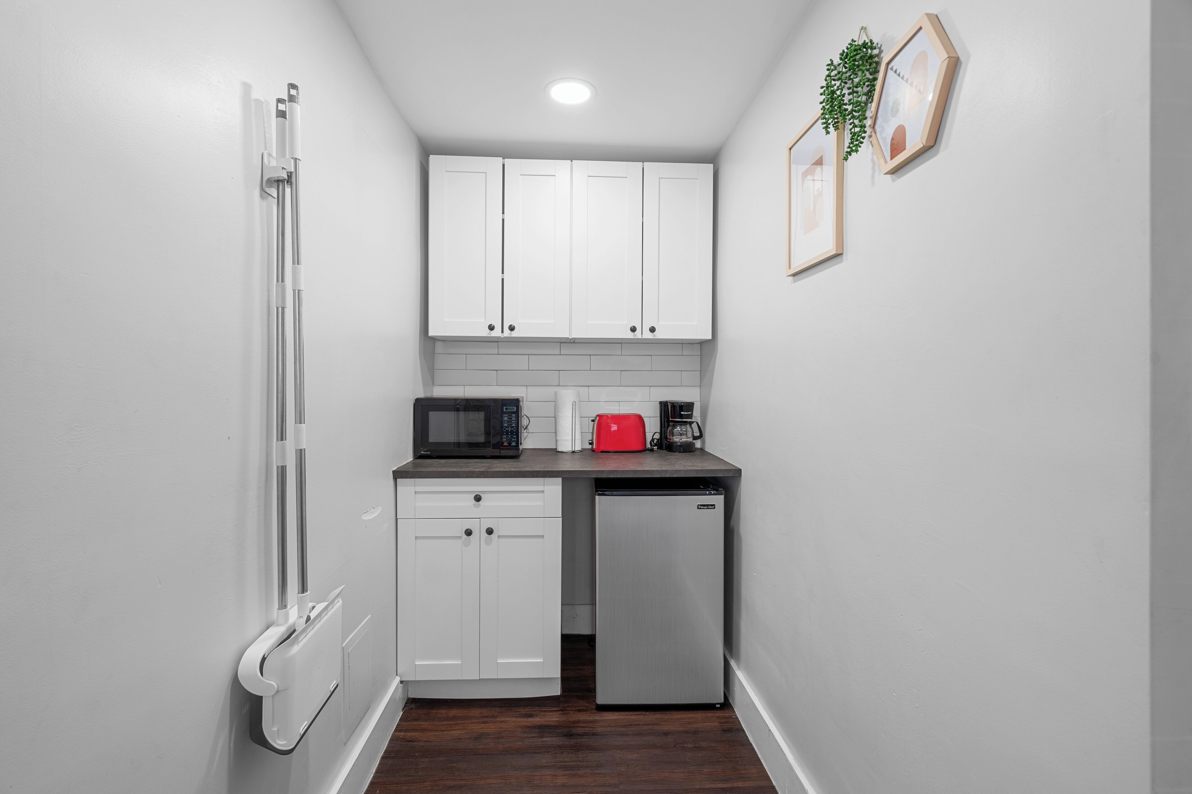 A compact kitchen with white cabinets, a microwave, a toaster, and a refrigerator.