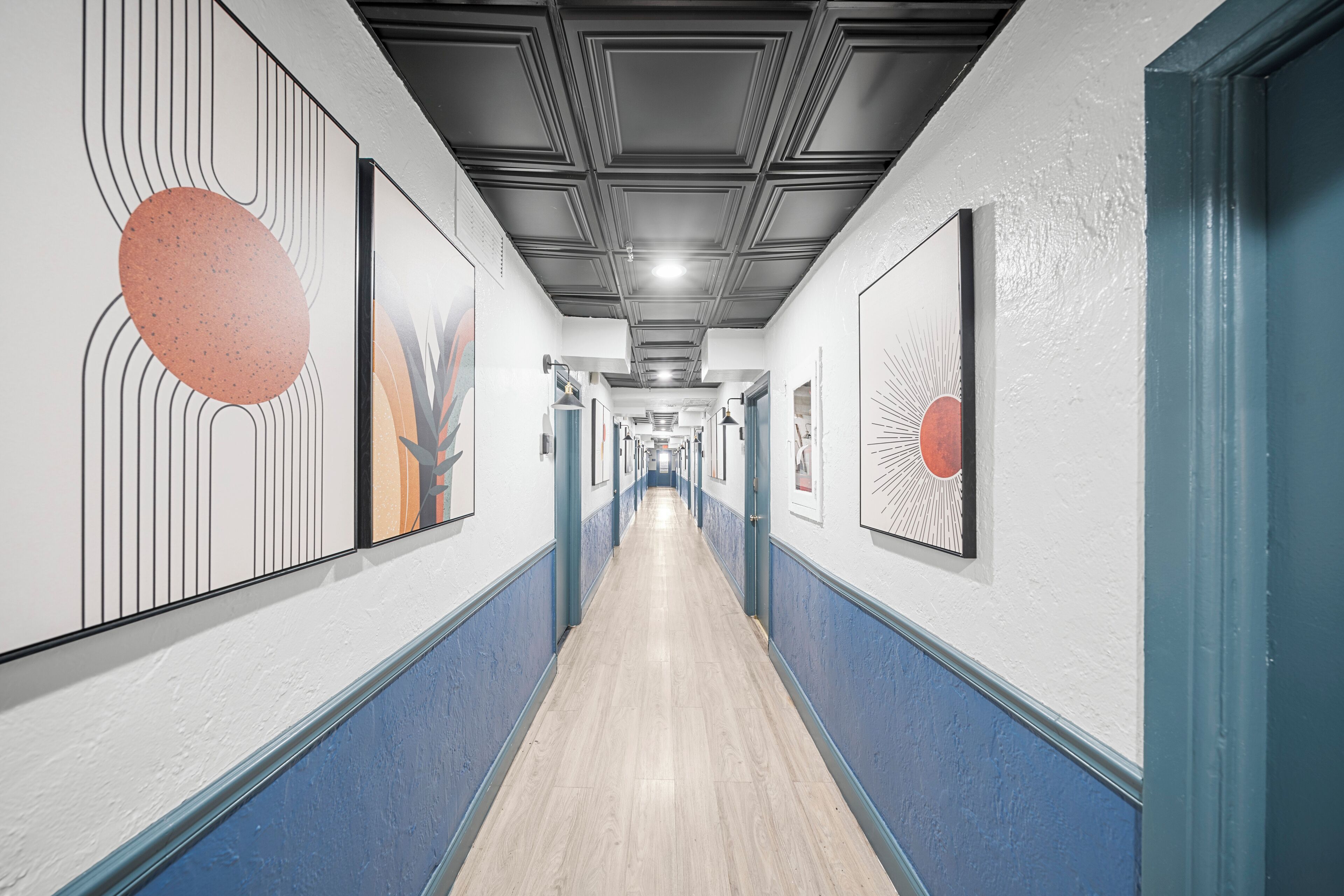 Un couloir dont les murs sont ornés d’œuvres d’art, avec un plancher en bois et un plafond à motifs géométriques.