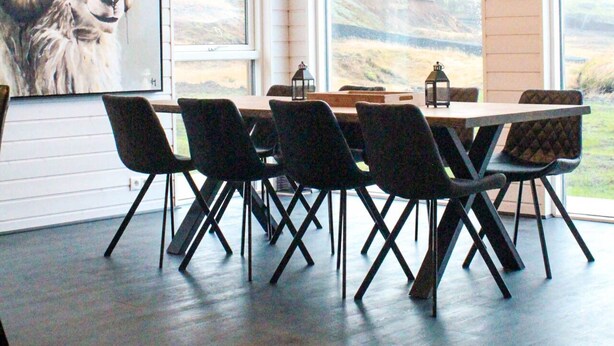 Ruokailutila, jossa on pöytä ja tuolit, suuret ikkunat ja eläimen kuva.