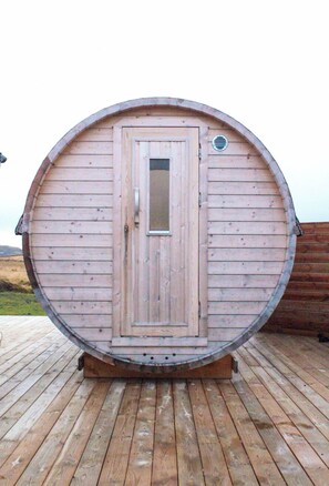 Un sauna en bois, doté d’une porte et d’une petite fenêtre, installé sur une terrasse en bois.