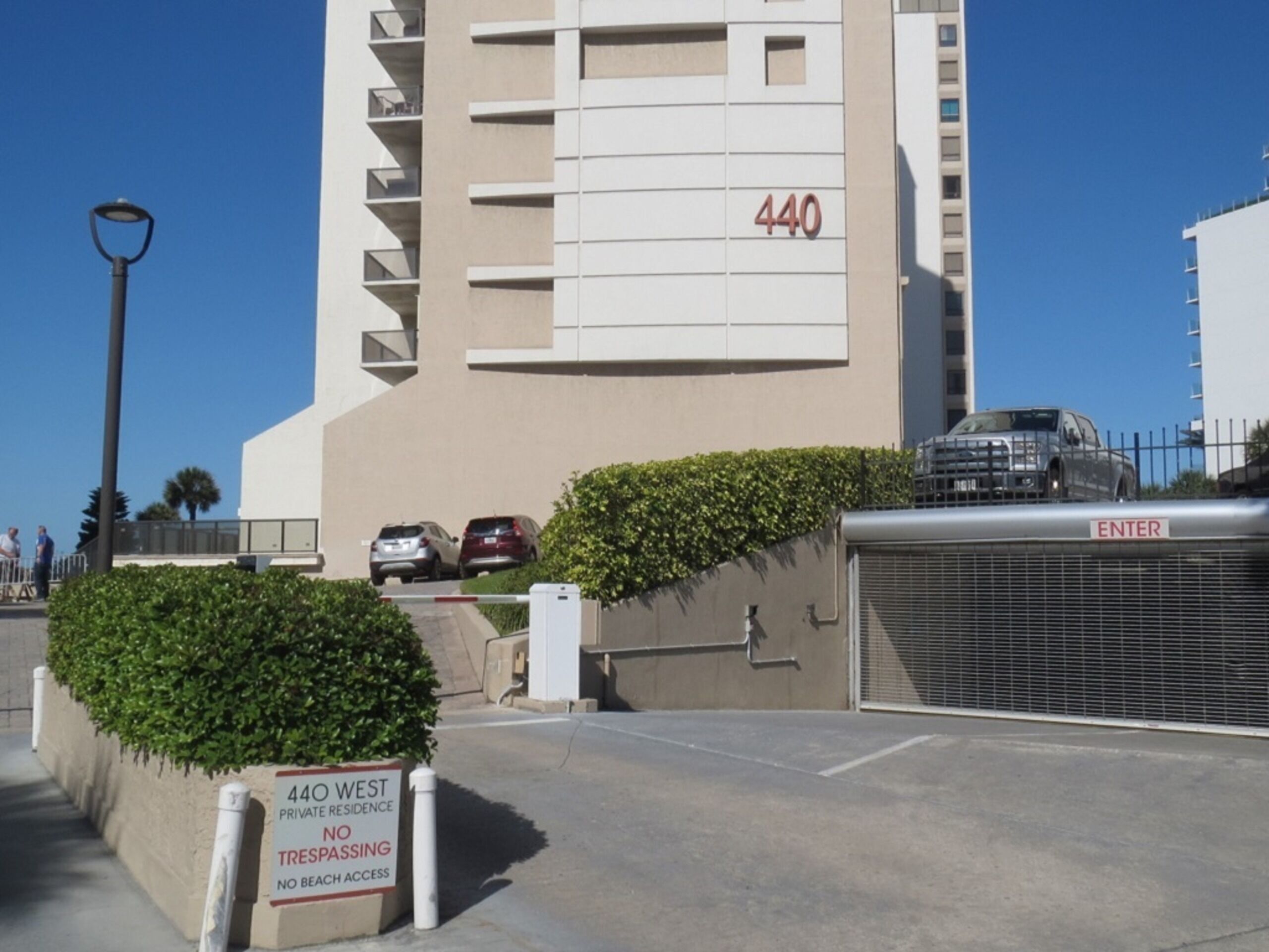 Un edificio moderno con el número 440 en su fachada, un acceso con portones y un letrero que indica que es una residencia privada, prohibido el acceso y sin acceso a la playa.