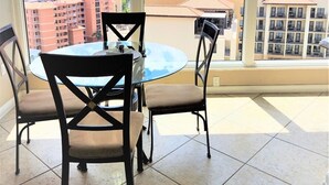 A balcony with a glass table and chairs, offering a view of the city and a body of water. - Beautiful Penthouse Style on Clearwater Beach (Clearwater)