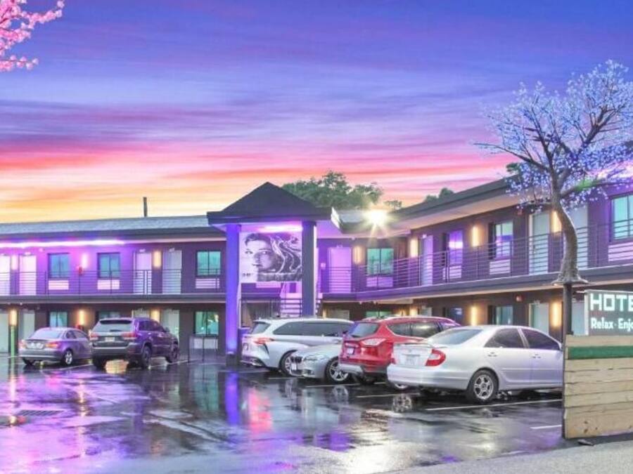 Un hotel con un cartel que dice "HOTEL CRUISER" y el lema "Relájate. Disfruta. Explora. Repite". Hay varios coches aparcados delante del hotel.