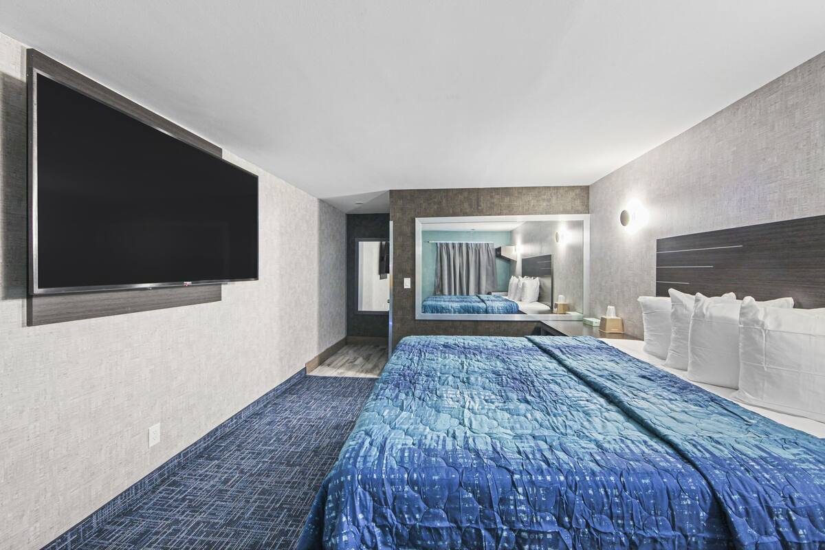 A modern hotel room with a large bed, a flat-screen TV mounted on the wall, and a bathroom visible through an open door.