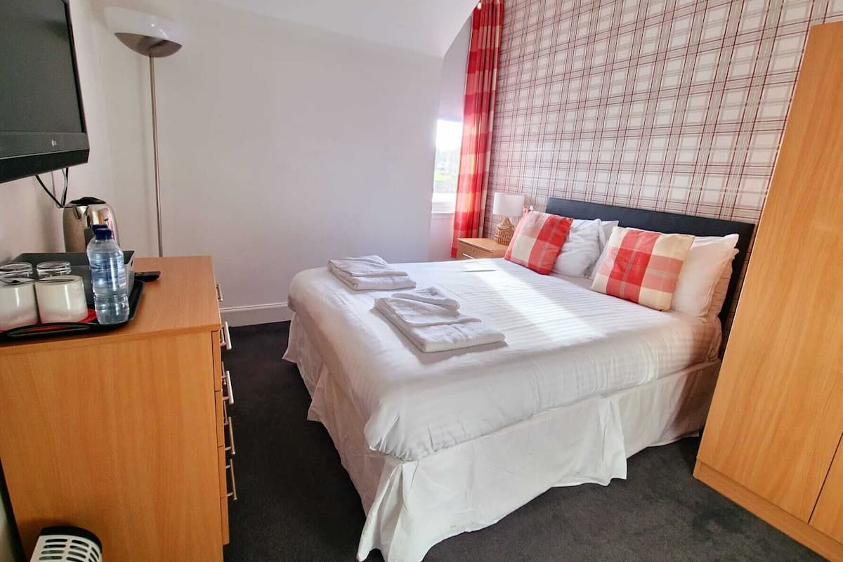 A hotel room with a bed, a desk with a computer, a TV, and a window with curtains.