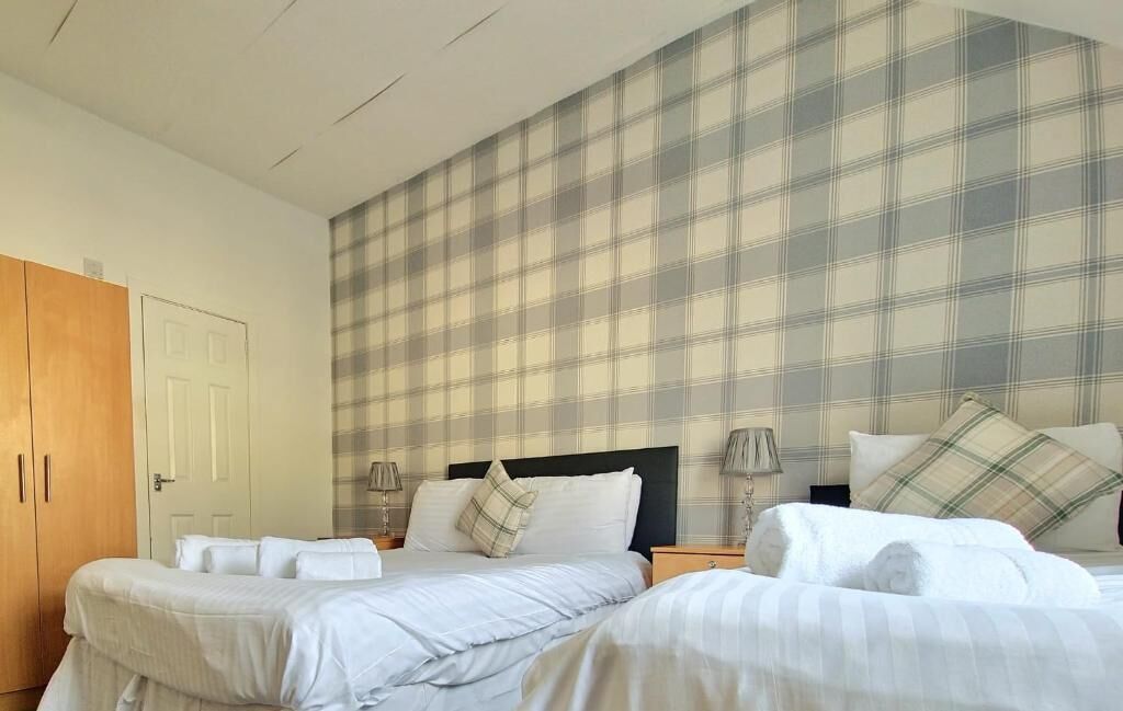 A hotel room with two beds, a wardrobe, and a plaid-patterned wall.