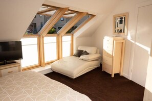 Un dormitorio con cama, cómoda, televisor y tragaluces.