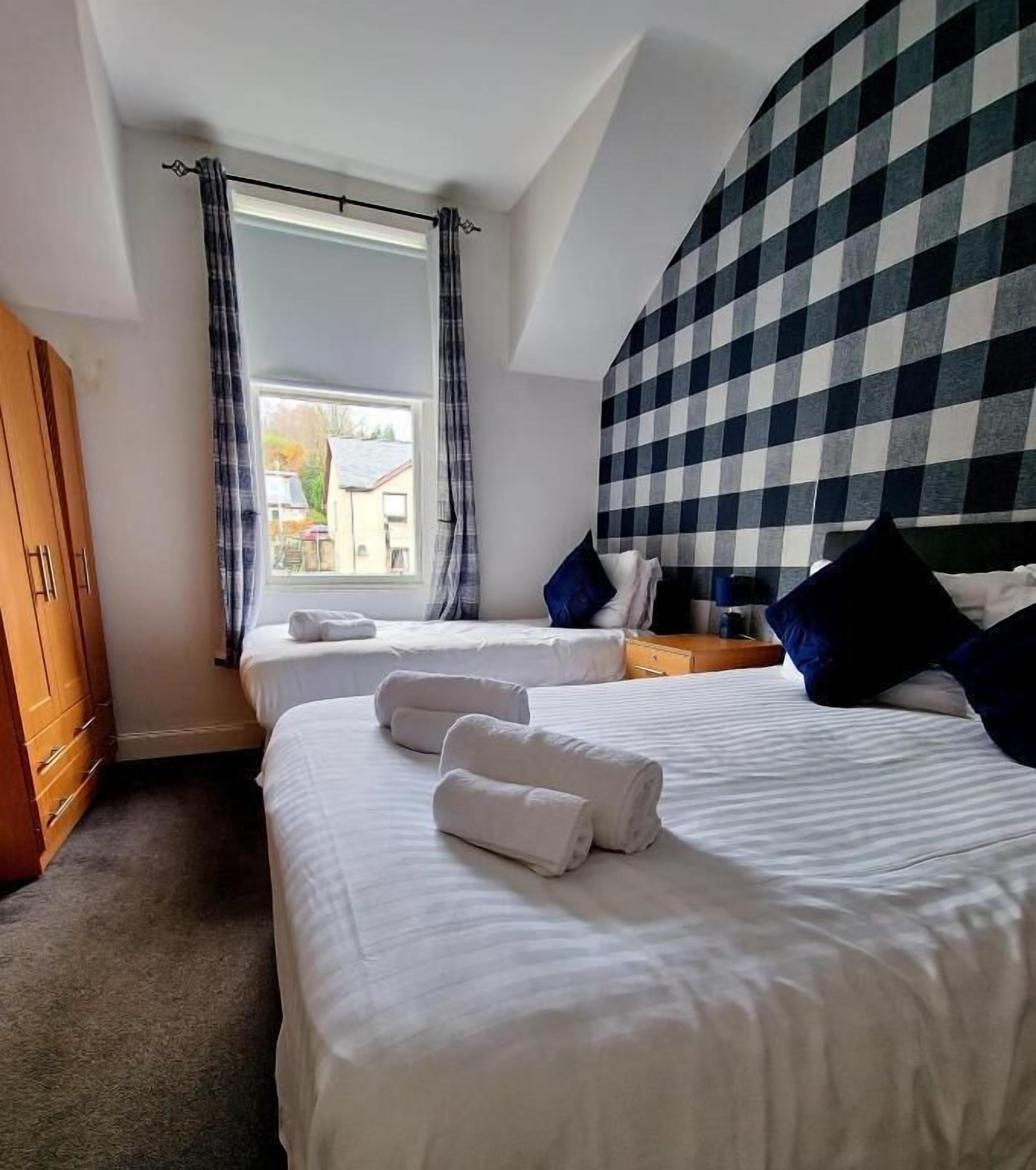 A hotel room with two beds, a window with curtains, a checkered headboard, and a wardrobe.