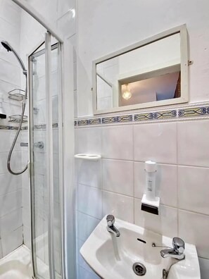 A bathroom with a glass shower enclosure, a sink with a soap dispenser, and a mirror above the sink.
