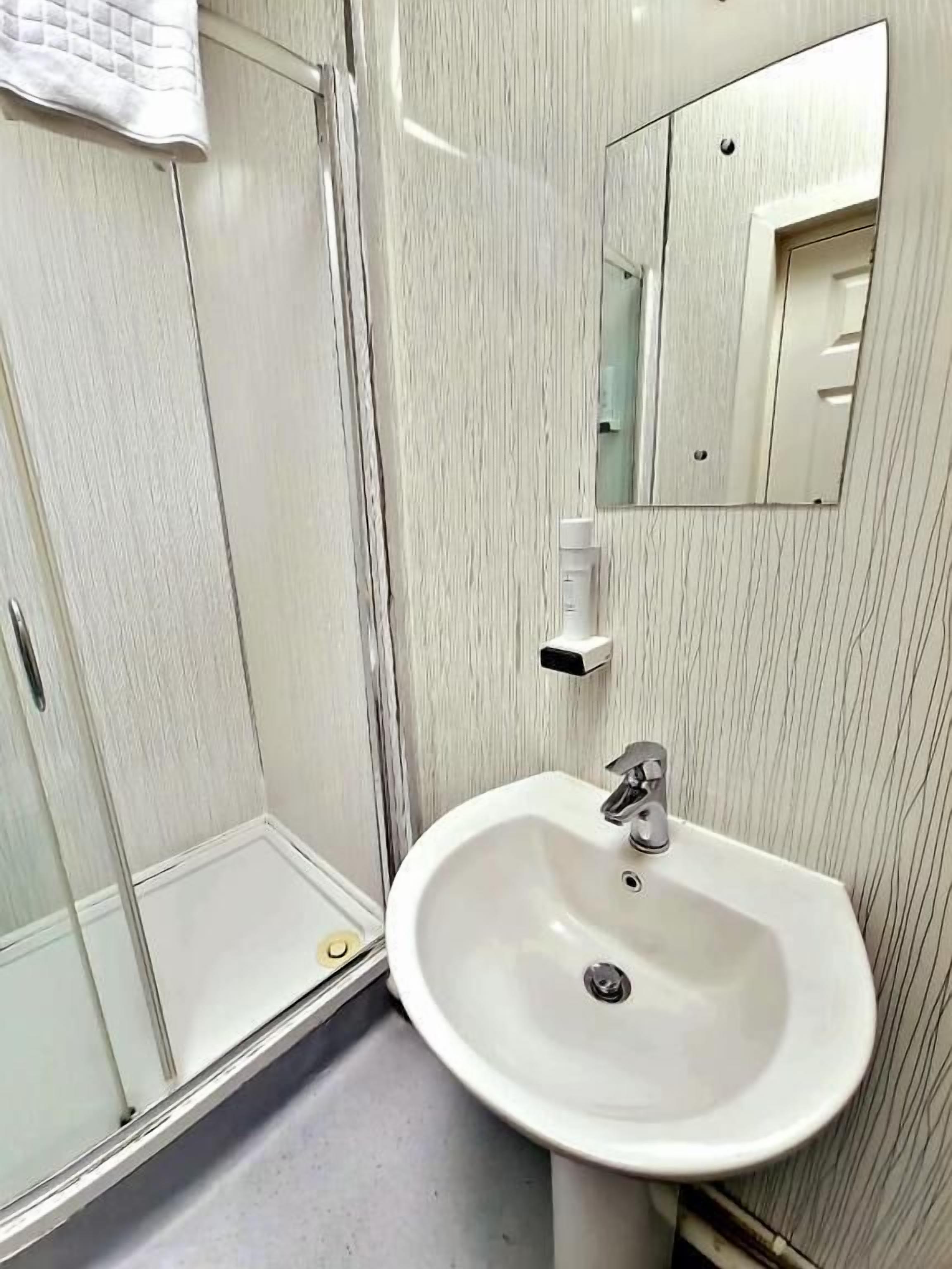 Une salle de bain avec un lavabo blanc, un miroir et une cabine de douche en verre.