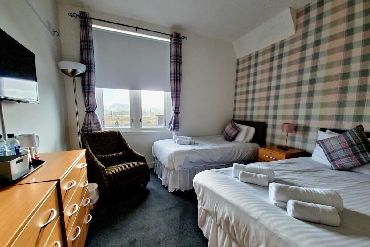 A hotel room with two beds, a wooden dresser, a chair, and a window with curtains.