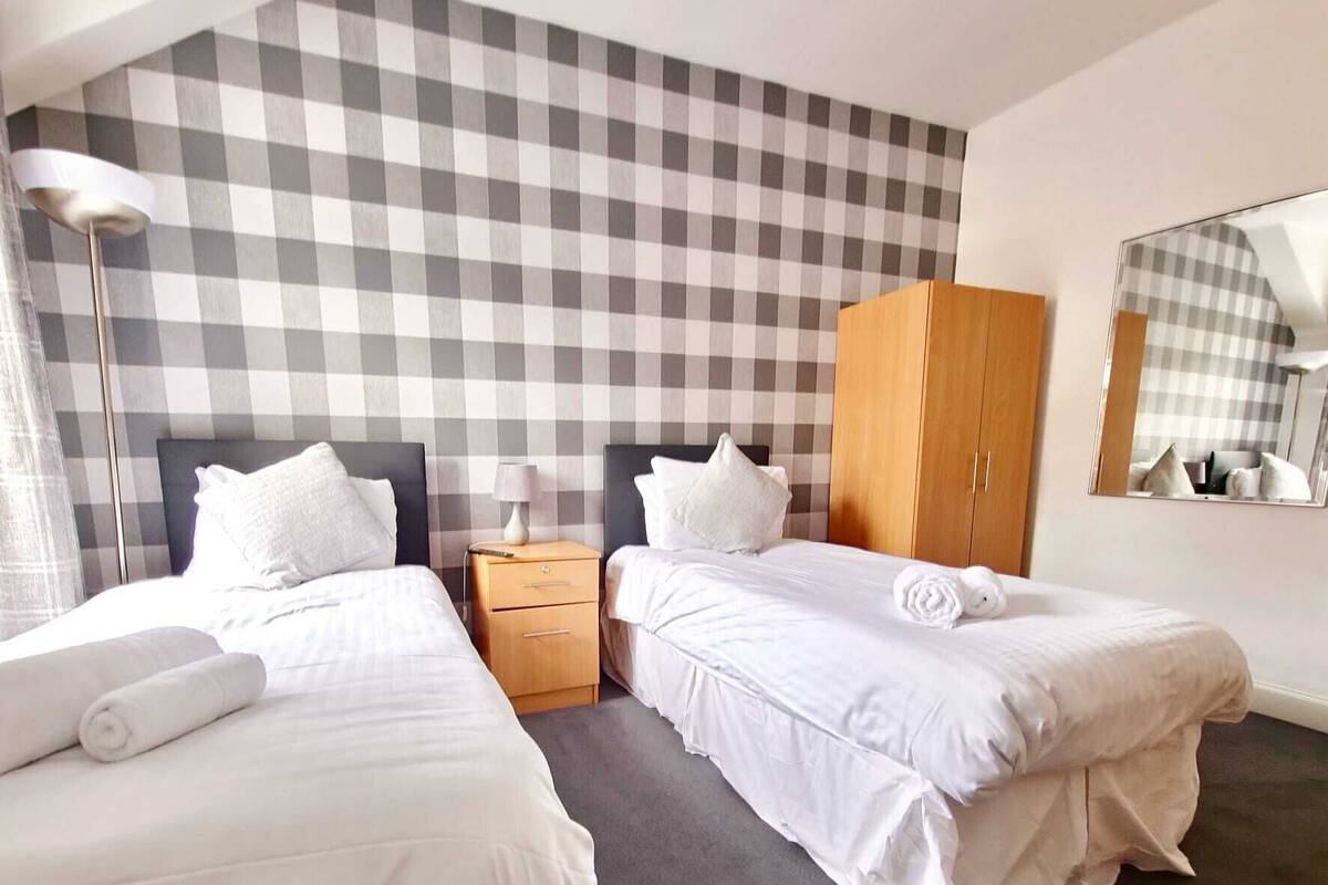 A hotel room with two beds, a wardrobe, a nightstand, a lamp, and a checkered wall.