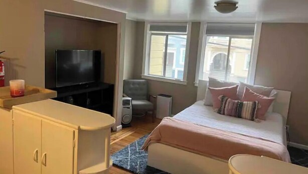 Un dormitorio con cama, televisor, una silla y un armario.