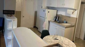 Cocina compacta con gabinetes blancos, un refrigerador, un lavamanos y un cartel anunciando degustación de vinos.