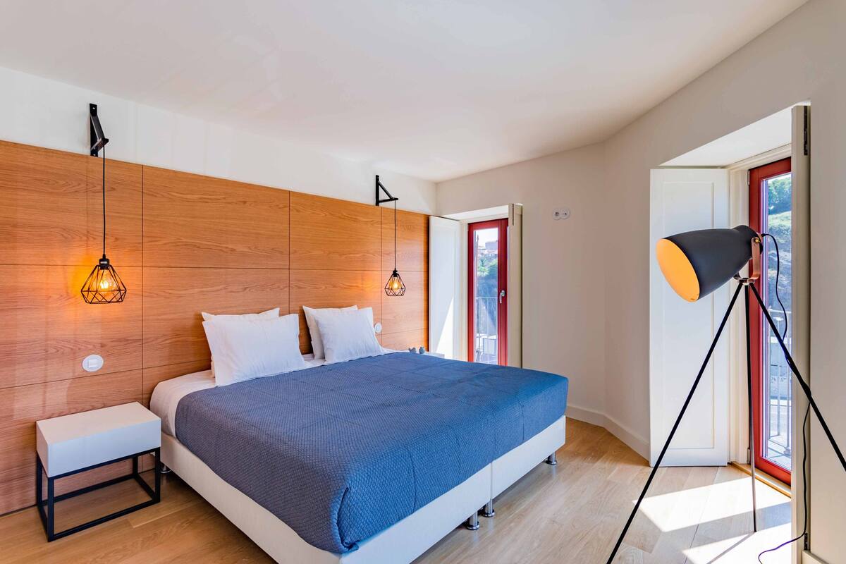 A modern bedroom with a wooden headboard, a bed with a blue blanket, bedside tables, and a floor lamp.