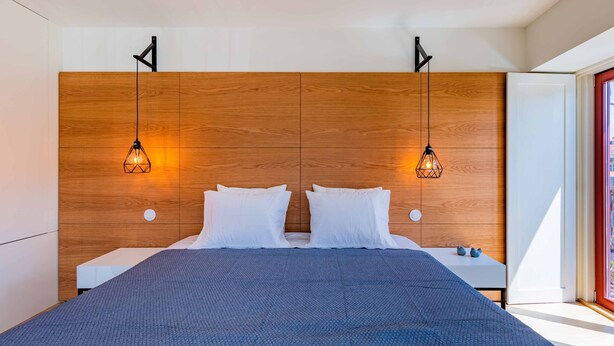 Un dormitorio moderno con una cabecera de madera, dos mesitas de noche y una cama grande con una colcha azul con textura.