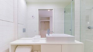 Un baño moderno con un lavamanos grande blanco, una cabina de ducha de vidrio y toallas ordenadas en un estante.