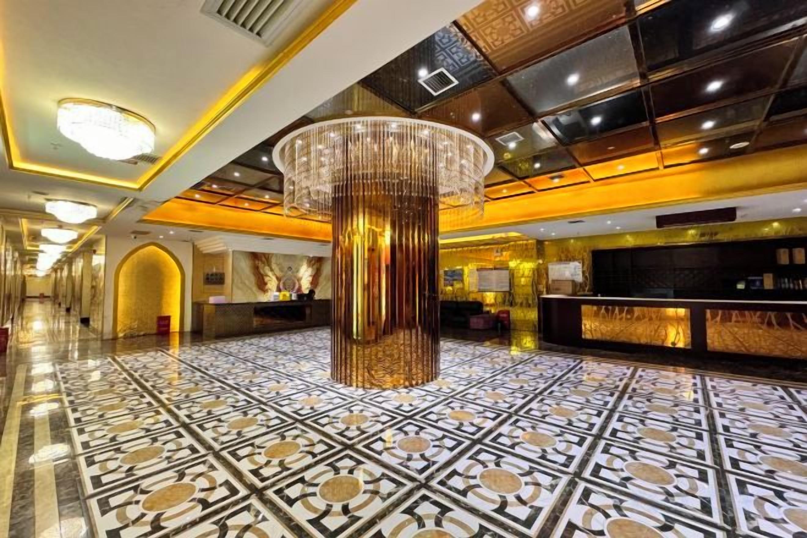 Eine Hotelhalle mit einem großen, verzierten Kronleuchter, einem Empfangsbereich und einem gemusterten Boden.
