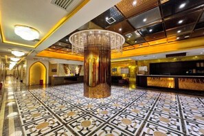 A hotel lobby with a large, ornate chandelier, a reception desk, and a patterned floor.