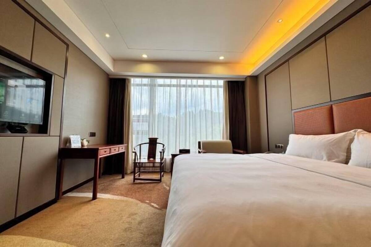 A hotel room with a large bed, a desk with a chair, a television, and a window with curtains.