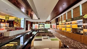 A modern hotel lobby with a central water feature, seating areas, and a variety of amenities including a reception desk and a food display.