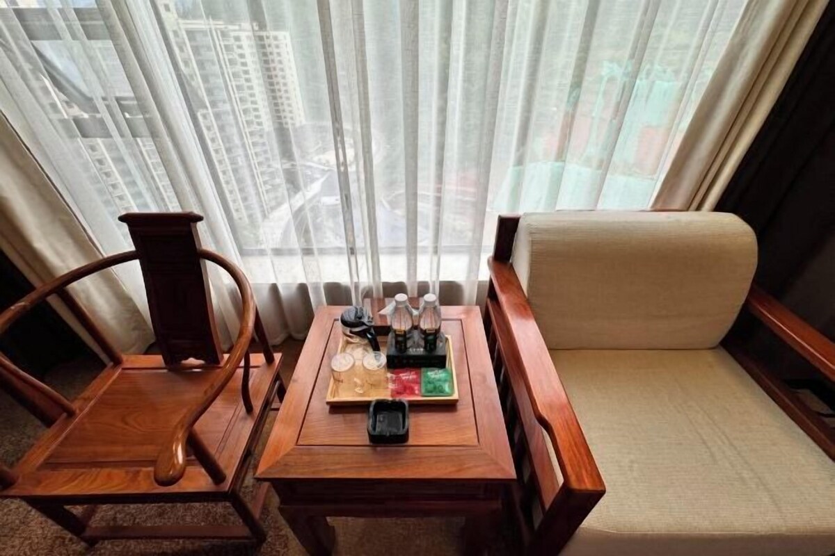 A hotel room with a wooden table, a chair, a sofa, and a window with curtains.