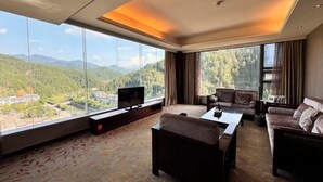 A modern hotel room with a large window offering a mountain view, a flat-screen TV, and a cozy seating area with a sofa and armchairs.