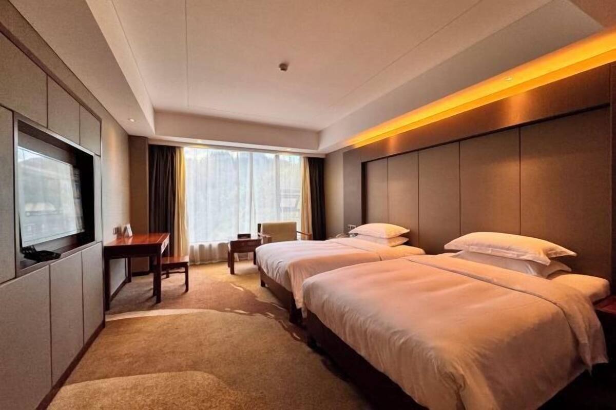 A hotel room with a large bed, a desk, a chair, and a TV.
