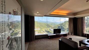 A modern hotel room with a large window offering a mountain view, a flat-screen TV on a stand, and traditional artwork on the wall.