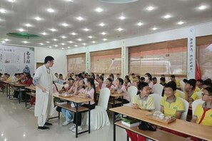 A classroom with students seated at desks, a teacher standing at the front, and educational posters on the walls.