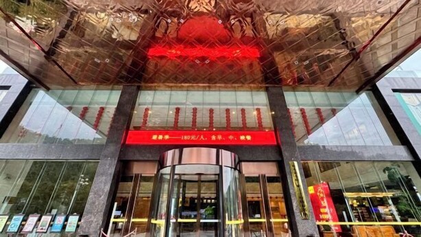 A modern building entrance with a glass facade, a red sign above the entrance, and a circular revolving door.
