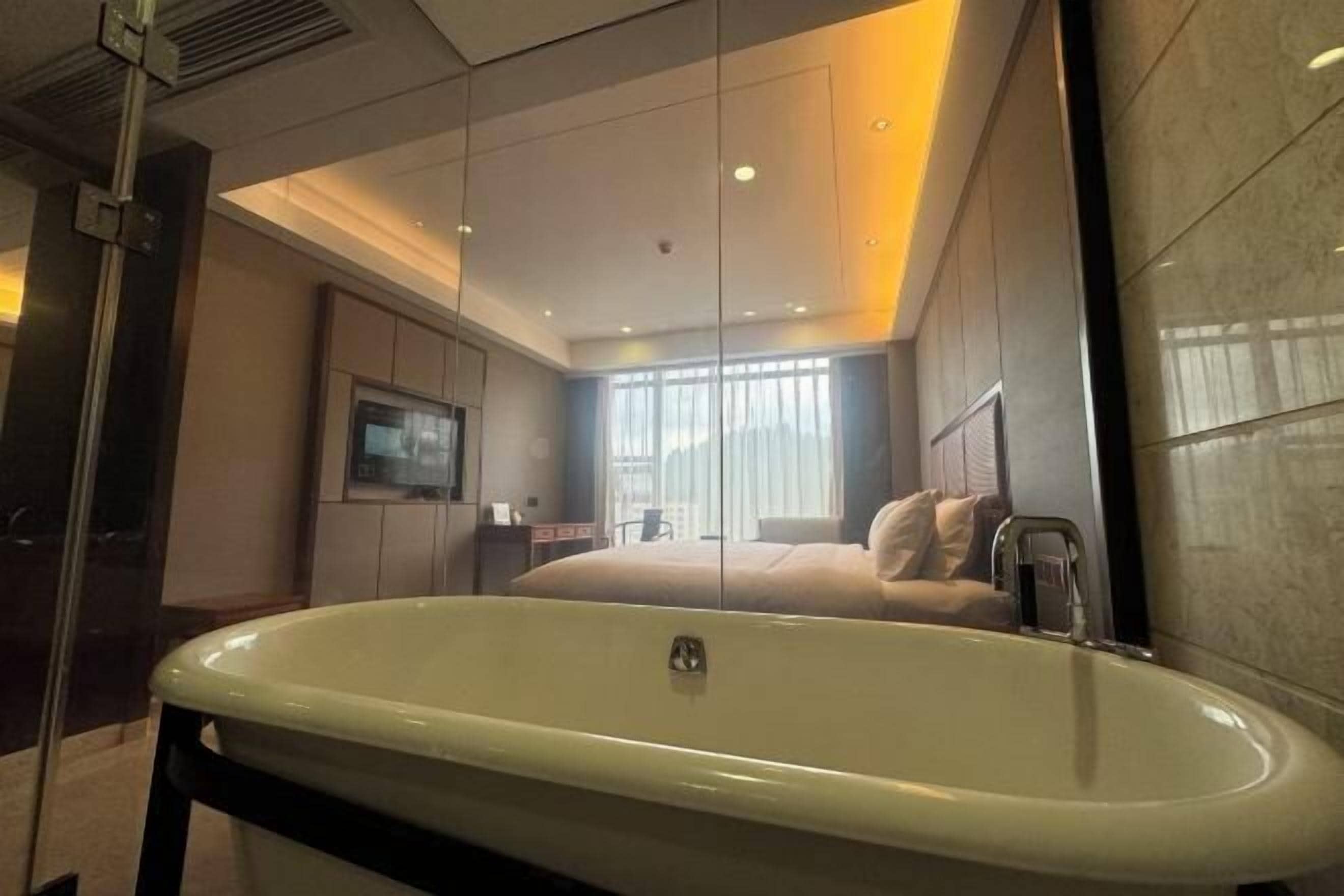 Una habitación de hotel moderna con una bañera grande, un televisor y un ventanal con cortinas.